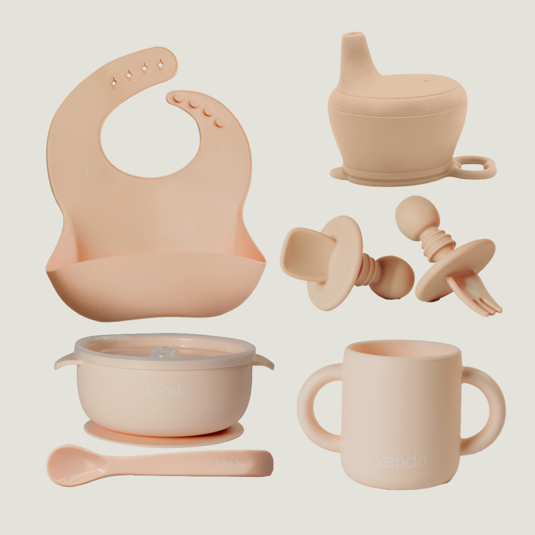 Set of baby feeding and teething products in pastel pink on a light beige background